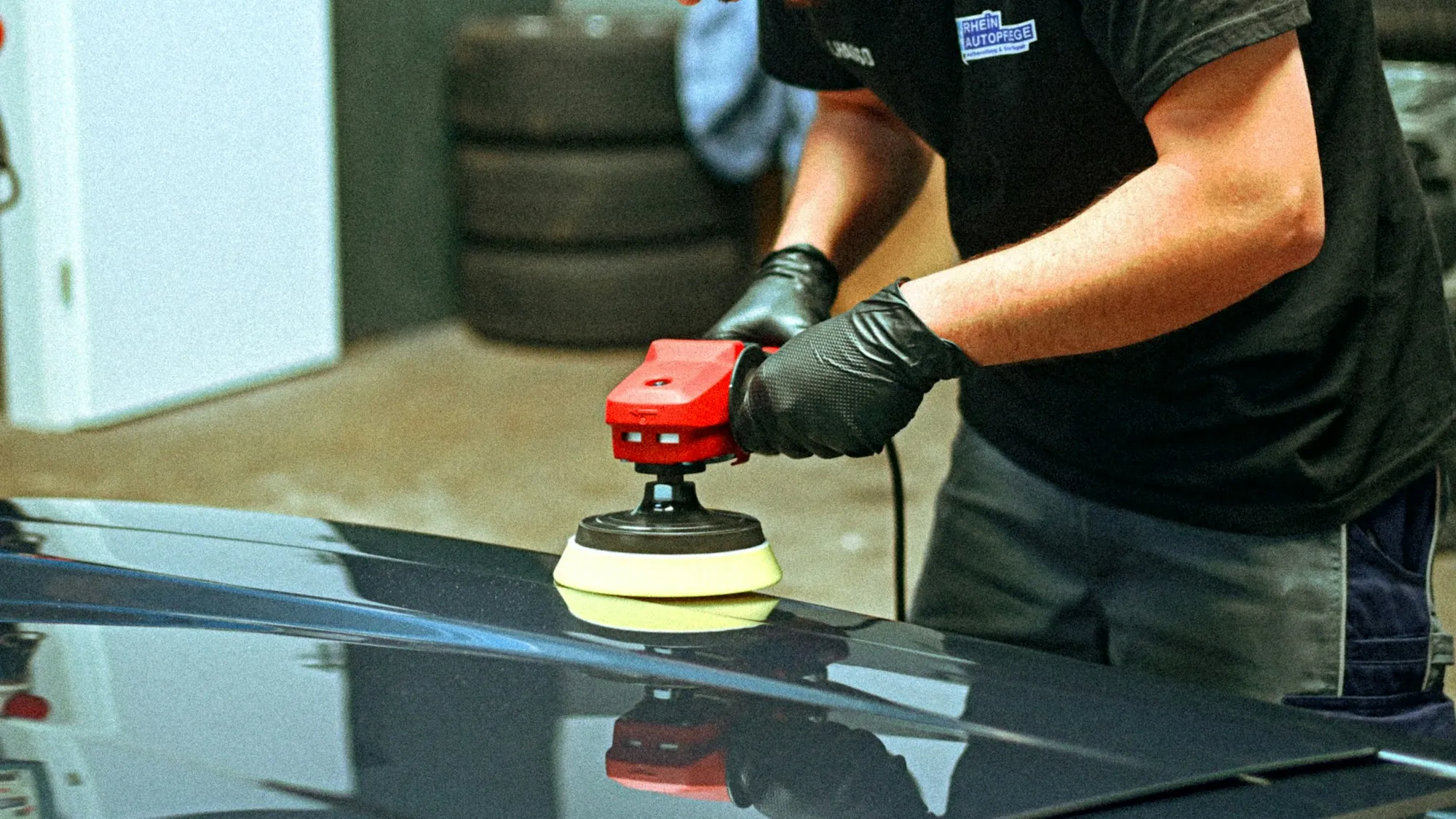 Technician machine polishing the hood of a dark car